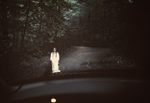 Spooky ghost in white standing in the middle of a dark road